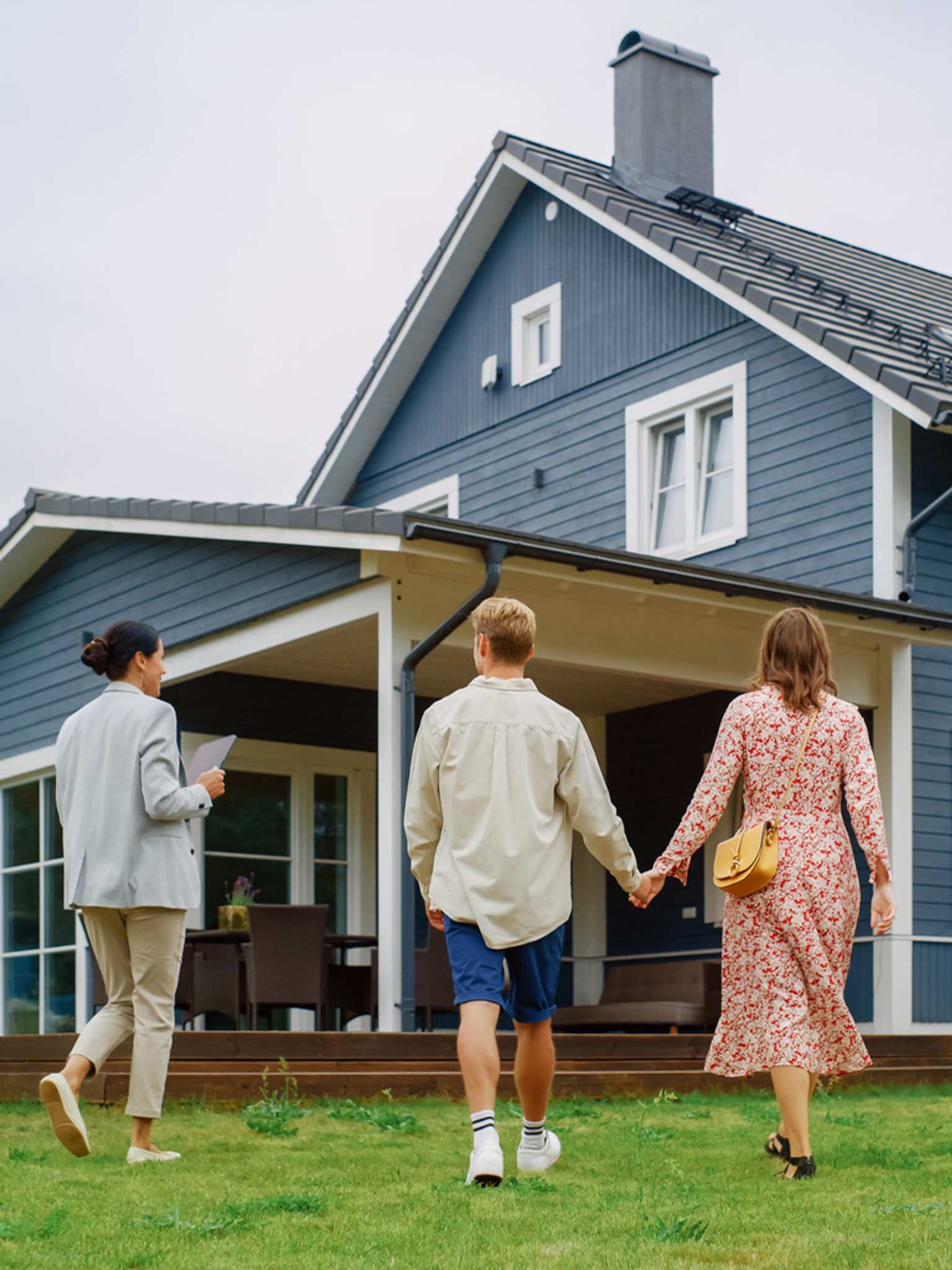 Three people walking towards a house, two holding hands, and one carrying documents.