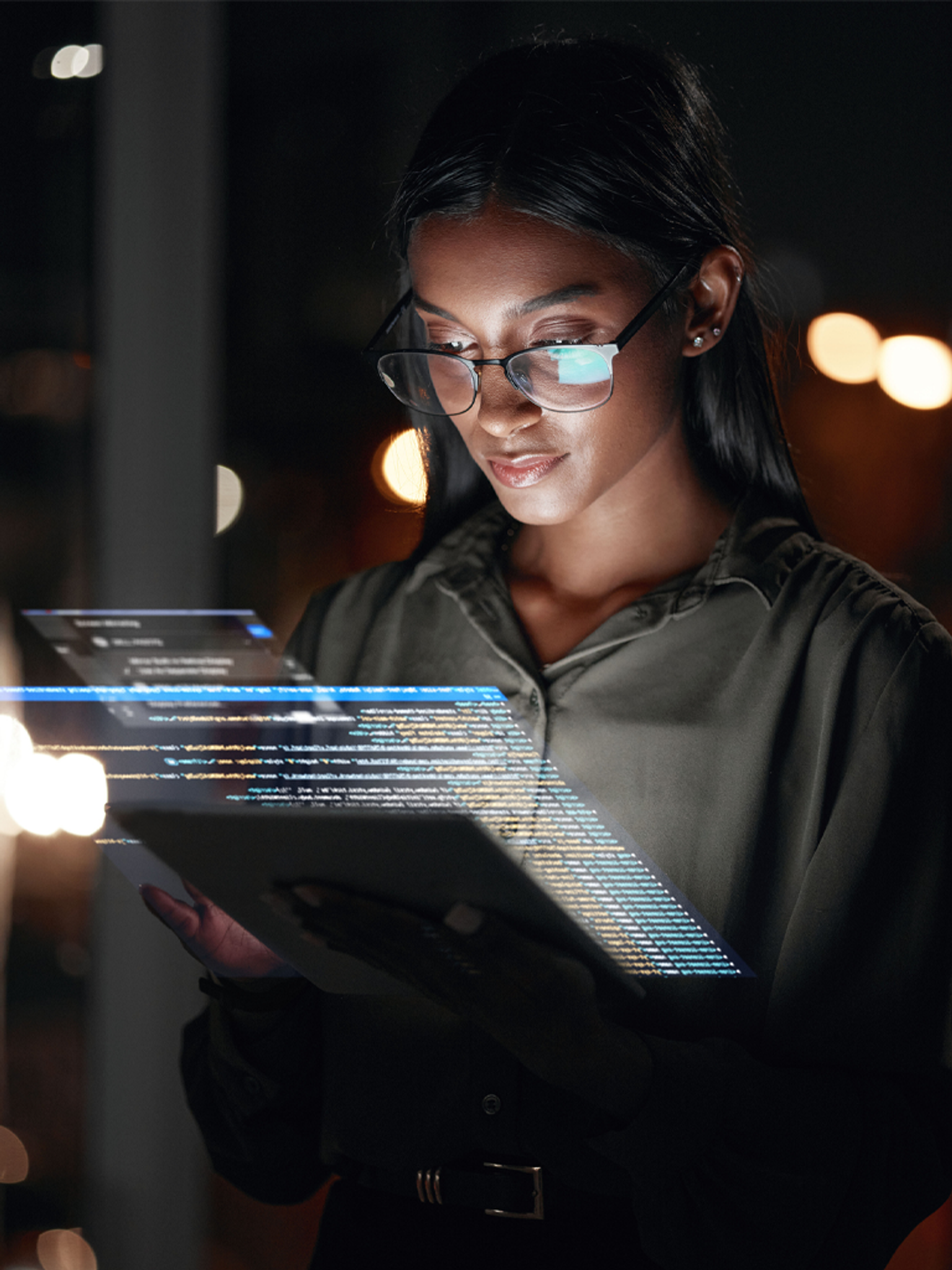 Woman analyzing holographic data projections from a tablet at night.