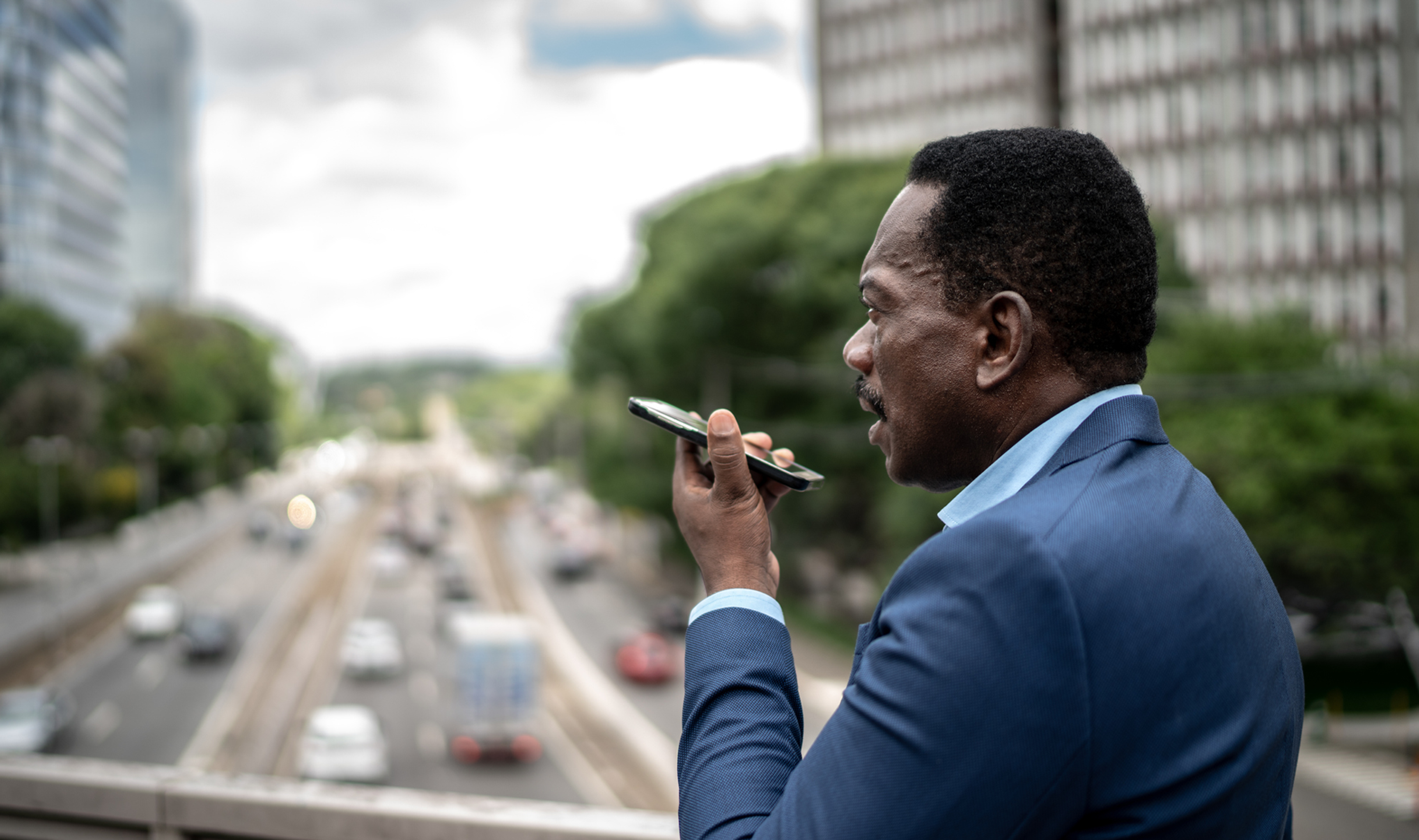 Man in suit using phone with city traffic in background.