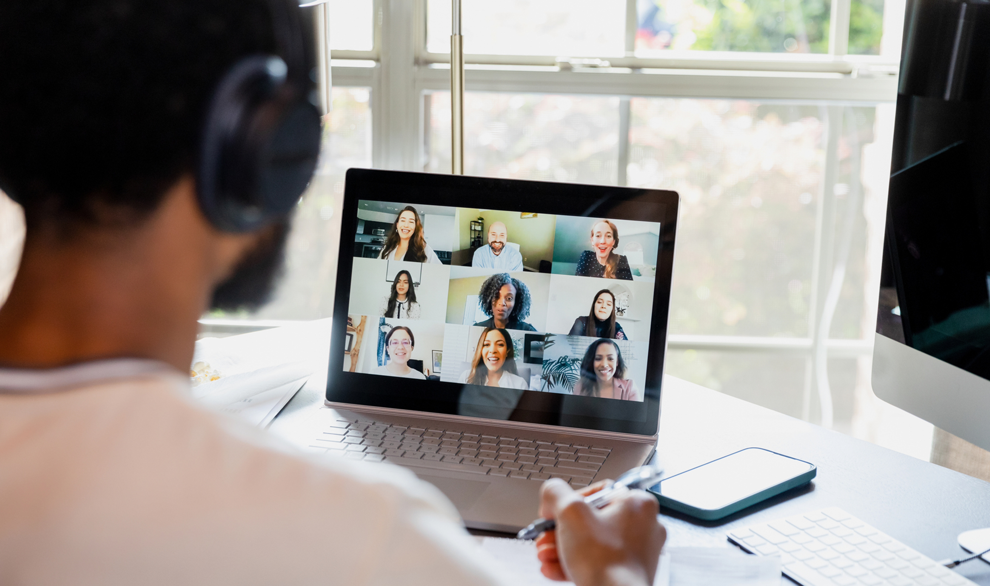 A person attending a virtual meeting with multiple participants on their laptop screen.