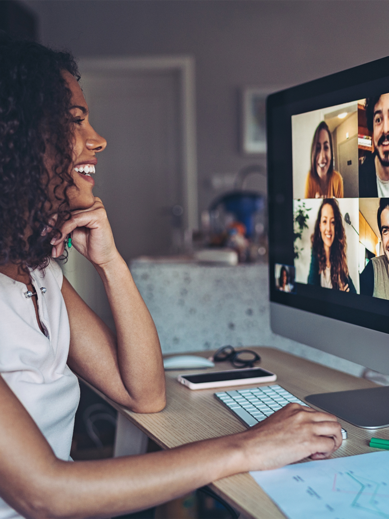 A woman smiles at a computer screen during a video call with three other people.