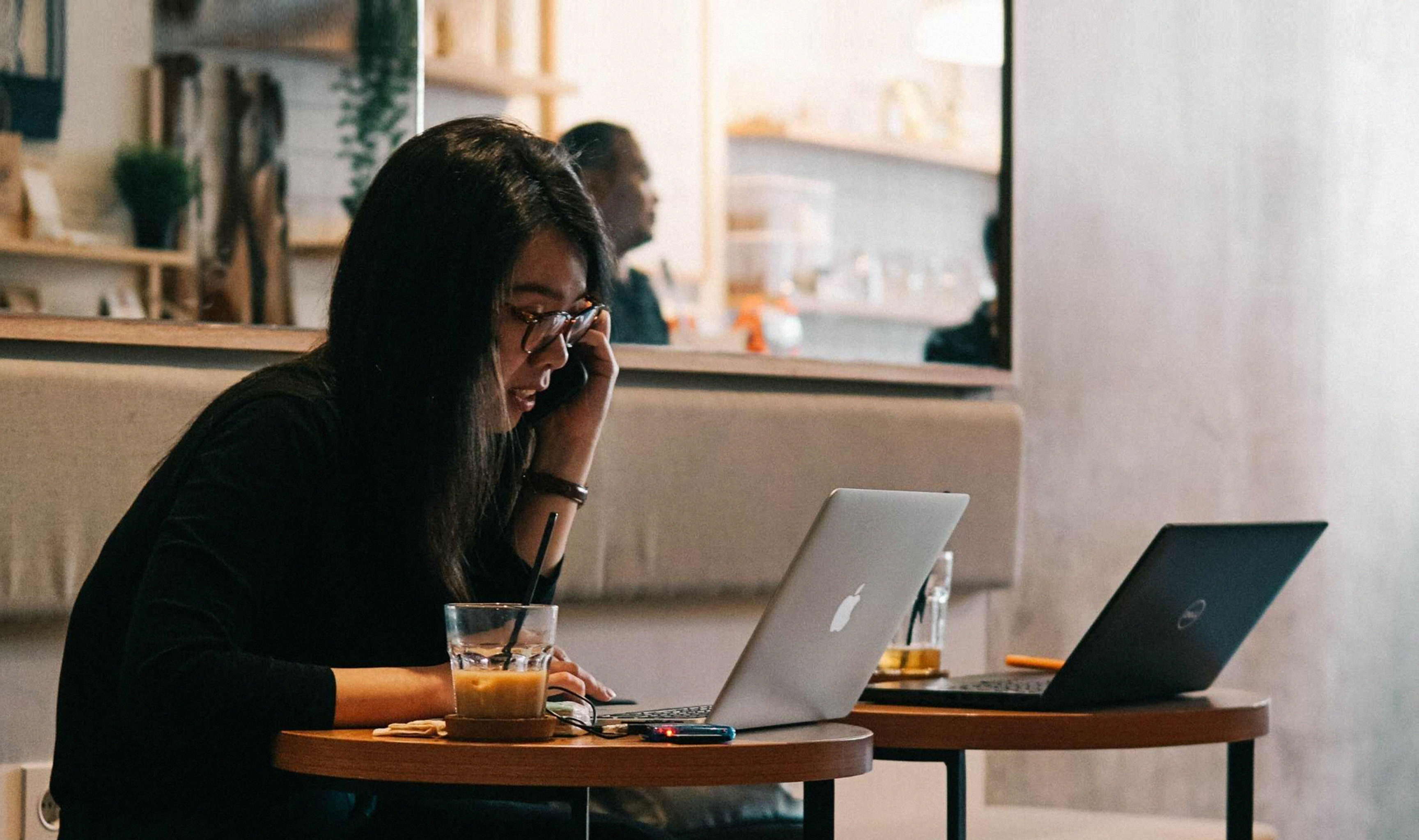 A person in a cafe working intently on a laptop with a beverage aside.