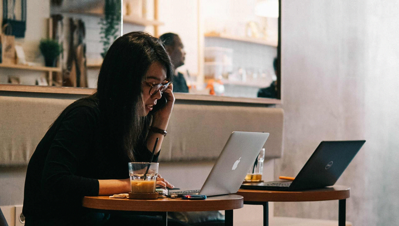 A person in a cafe working intently on a laptop with a beverage aside.