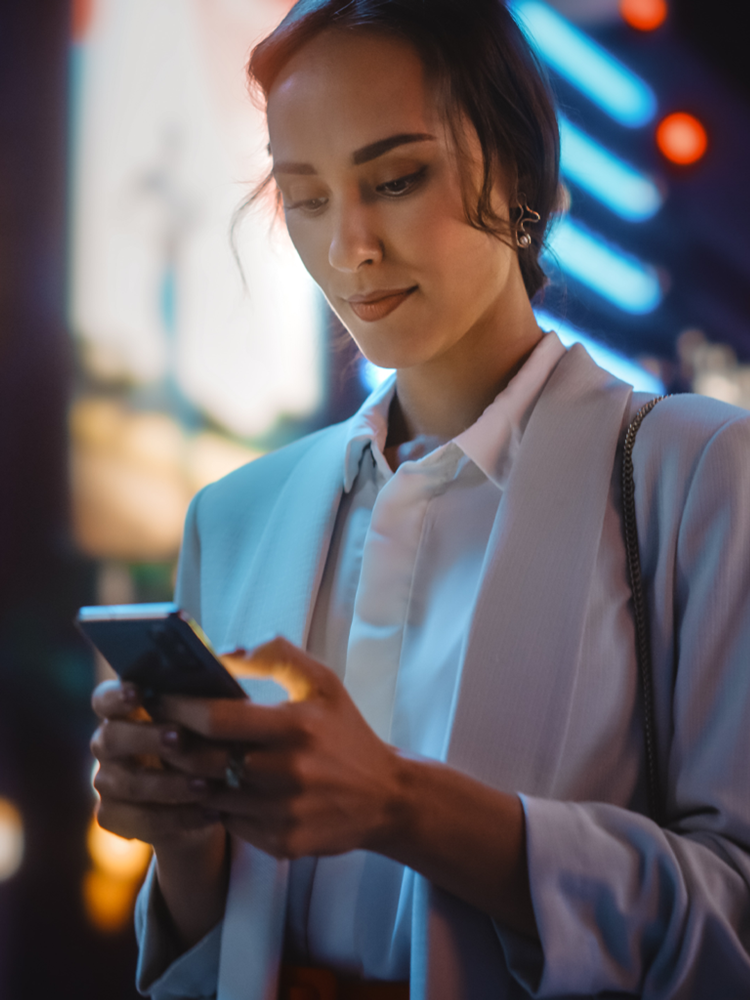 A woman focused on her phone with colorful neon lights in the background.