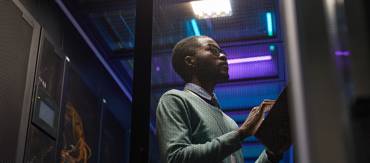 A person with a clipboard inspects a server room, illuminated by blue lights.